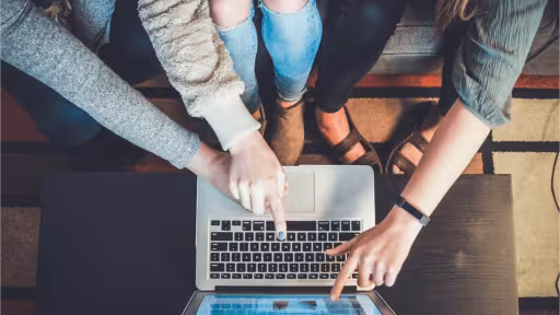 Three people sitting on a couch pointing at a laptop.